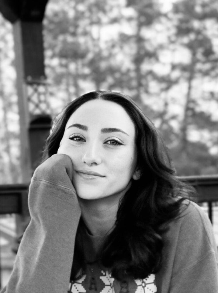 Black and white portrait of a woman resting her face on her hand outdoors.