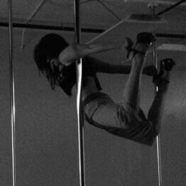 Person pole dancing with dumbbells in hand.