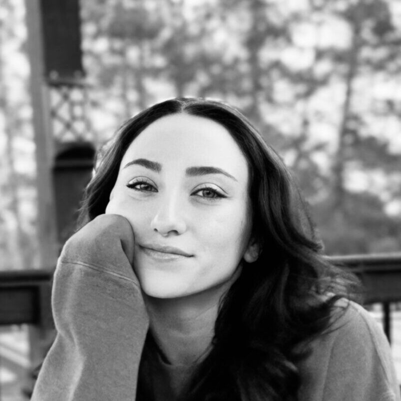 Black and white portrait of a woman resting her face on her hand outdoors.