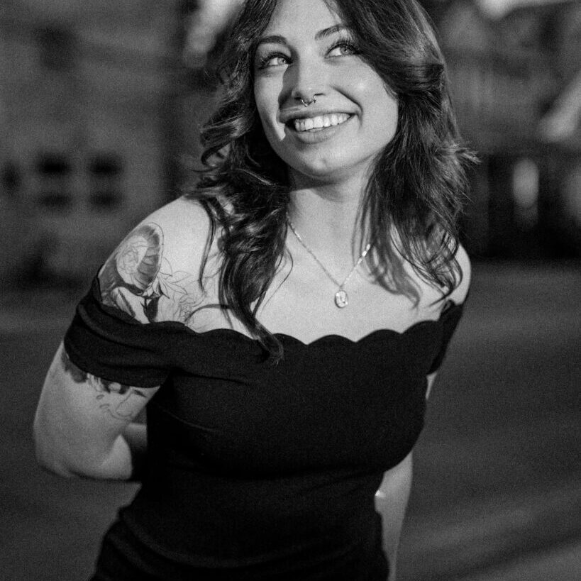 Black and white photo of a smiling woman in an off-shoulder dress.